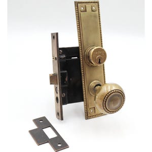 以下が含まれることがあります： 装飾的な長方形のバックプレート、丸いドアノブ、鍵穴を備えた、ヴィンテージの真鍮製ドアロックセット。 セットには、別のストライクプレートと内部ロック機構が含まれています。 仕上げは経年変化しています。