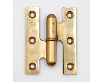 May include: A brass H-hinge with rounded ends and a central barrel. Each leaf has four screw holes. The hinge has a tarnished appearance and the letters "TTS" are stamped on one leaf.