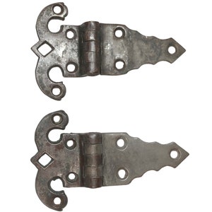 May include: A pair of antique iron hinges with ornate designs. The hinges are in a worn, rustic finish and have a decorative, pointed shape on one side.