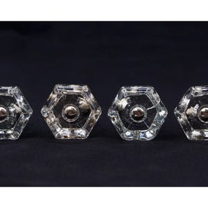 May include: Four clear glass hexagonal cabinet knobs with a silver metal center.