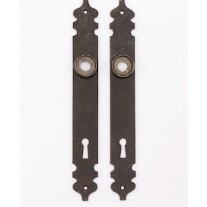Puede incluir: Dos placas de puerta de estilo antiguo con una cerradura y un pomo redondo. Las placas son de metal oscuro y tienen un diseño decorativo.