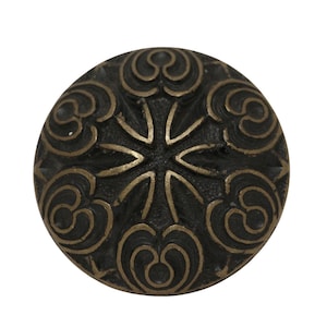 Peut inclure: Un bouton rond en métal noir avec un motif orné de couleur dorée. Le motif présente un étoile centrale avec des motifs tourbillonnants autour.