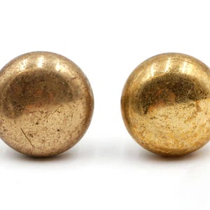 May include: Two antique brass spheres with a worn, textured surface. The spheres have a golden hue and are set against a white background. These decorative spheres could be used as furniture hardware or decorative accents.