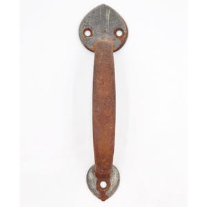 May include: A rustic, weathered door pull with a heart-shaped backplate and handle. The metal hardware has a distressed, rusty brown finish, with a gray backplate. The door pull is designed for easy gripping.