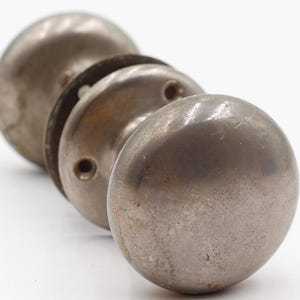 Puede incluir: Primer plano de cuatro pomos de puerta metálicos antiguos. Los pomos son de color plateado deslustrado y de forma redonda. Los pomos están dispuestos en fila, con el más cercano enfocado. El fondo es blanco.