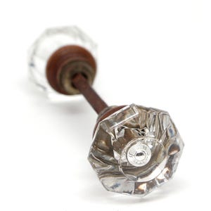 Könnte beinhalten: Ein klarer, facettierter Türknauf aus Glas mit einem rostbraunen Metallschaft und -fuß. Der Knauf hat ein klassisches, Vintage-Design und ist vor einem weißen Hintergrund platziert. Das Glas ist transparent.