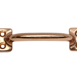 Puede incluir: Una manija de puerta de color cobre con forma redondeada y dos agujeros a cada lado. La manija está diseñada para tirar de las puertas.