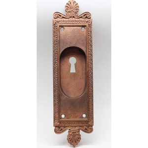 Peut inclure: Une plaque de serrure vintage en cuivre orné avec une bordure décorative et un trou de serrure au centre.