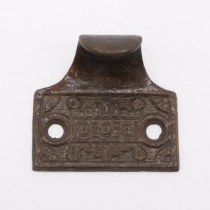 May include: A vintage window sash lift with a decorative design and the text "S.M. & CO. PATENTED" on the front. The lift is made of metal and has a brown patina.