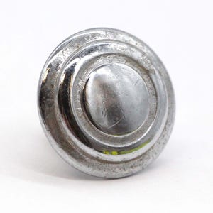 Peut inclure: Un bouton rond argenté avec un motif de cercles concentriques. Le bouton a une finition lisse et brillante.
