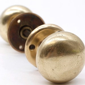 May include: A pair of brass door knobs with a round, slightly textured design. The knobs are attached to a brass plate with a keyhole.