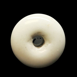 May include: White ceramic button with a raised center and a hole in the middle.
