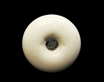 May include: White ceramic button with a raised center and a hole in the middle.