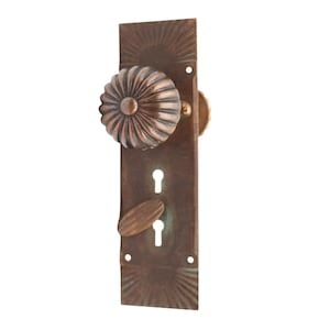 Può includere: Un set di maniglie per porte in bronzo antico. Il set include una maniglia decorativa e scanalata e una placca posteriore abbinata con un buco della serratura e una piccola leva di forma ovale. La placca posteriore ha un design a raggiera.