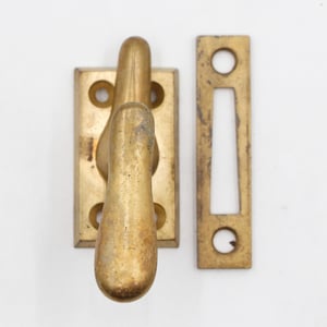 May include: A vintage brass door latch set. The set includes a rectangular plate with a curved handle and a separate rectangular strike plate. The brass has a warm, aged patina, suggesting its antique nature.