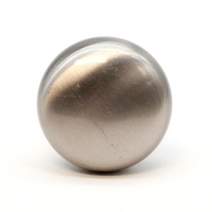 May include: A round, silver-toned cabinet knob with a smooth, brushed finish.
