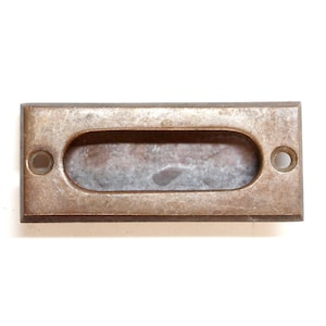 May include: A rectangular, brass-colored drawer pull with a long, oval-shaped cutout. The pull has a slightly worn, aged look.