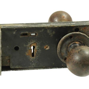 May include: A vintage door lock and handle set with a keyhole and two round knobs. The metal is dark brown and shows signs of wear and rust.