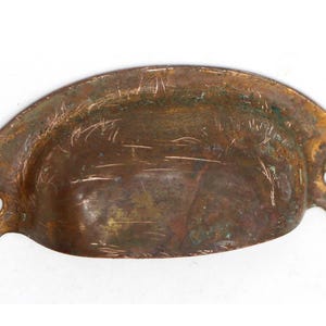 May include: A vintage copper drawer pull with a rounded, oval shape and two small holes for mounting. The pull has a worn, aged patina.