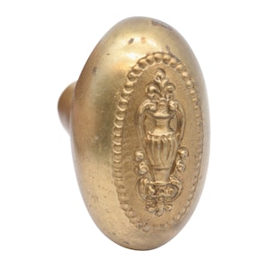 May include: A gold-toned door knob with an oval-shaped design featuring an ornate, embossed floral pattern with a vase in the center.