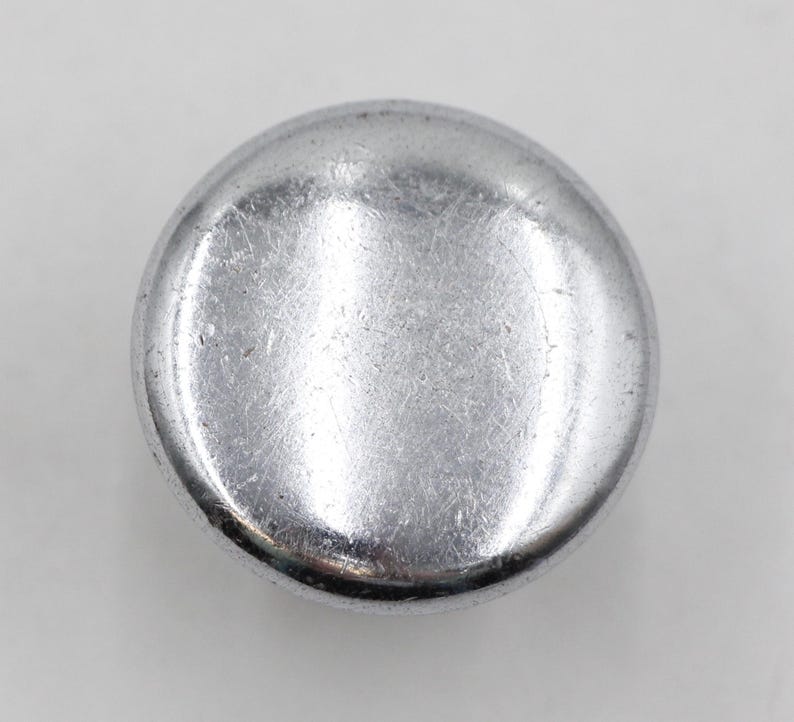 May include: A silver-coloured metal button with a smooth, slightly rounded surface.