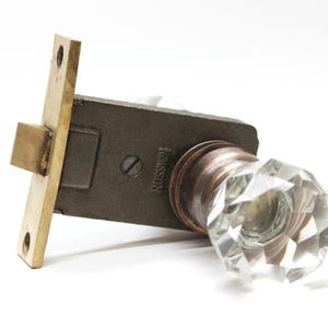 May include: A vintage brass door knob with a clear glass faceted knob. The knob is attached to a brass plate with a black metal latch. The plate has the word "RUSSWIN" embossed on it.