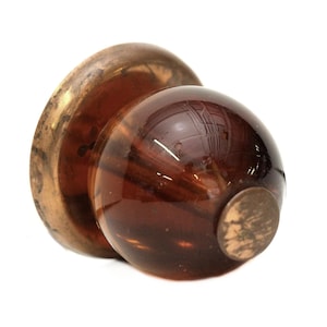 May include: A brown glass cabinet knob with a gold metal base. The knob has a round shape and a smooth surface.