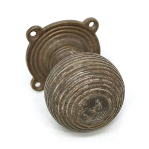 Puede incluir: Un pomo de puerta de latón vintage con un diseño redondo y acanalado. El pomo está unido a una base circular con un patrón decorativo de anillos concéntricos.