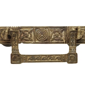 Może przedstawiać: Złoty metalowy uchwyt do szuflady z ozdobnym wzorem. Uchwyt ma prostokątny kształt z podniesioną częścią środkową i dwoma ozdobnymi elementami bocznymi.