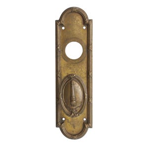 May include: A brass door plate with an ornate design and a keyhole. The plate has a decorative oval shape with a floral design.