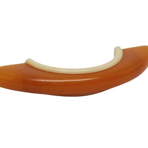 Puede incluir: Un anillo de plástico marrón y blanco con una superficie lisa y redondeada. El anillo está diseñado para ser utilizado como protector de dedos para tocar la guitarra.