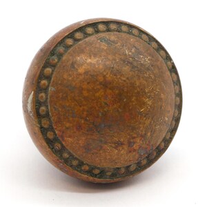May include: A round, brass door knob with a beaded edge. The knob has a worn, aged finish.
