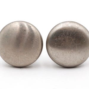 May include: Two brushed metal cabinet knobs with a rounded, spherical design. The knobs are a muted silver color and have a slightly textured surface. They are set against a white background.