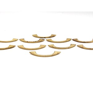 May include: Ten gold-toned metal cabinet pulls with a curved, slightly pointed design.