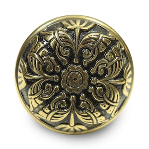 Peut inclure: Bouton rond de style ancien avec un motif floral orné. Le bouton présente un centre sombre, peut-être oxydé, avec des détails en relief de couleur or. Les bords sont également dorés, créant un contraste.