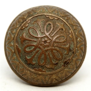 May include: Vintage bronze door knob featuring an ornate floral pattern. The circular knob has a central floral design and a decorative border. The bronze has a patina with green hues.