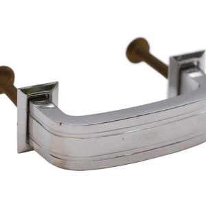 May include: A chrome cabinet pull with a rectangular shape and a grooved design. The pull has two brass screws.