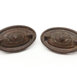 May include: Two antique oval-shaped cabinet pulls with a decorative floral design and a raised center knob. The pulls are made of a dark metal with a rustic finish.