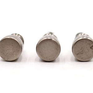 Op de afbeelding: Drie kleine, zilverkleurige decoratieve flessen met afgeronde bodems en smalle halzen zijn horizontaal geplaatst tegen een witte achtergrond. De flessen lijken van metaal te zijn en hebben een eenvoudig, elegant ontwerp.