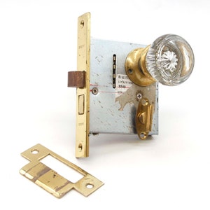 May include: A brass door lock set with a clear glass doorknob. The lock has a label that reads "Baldwin Lock Supply 8540".