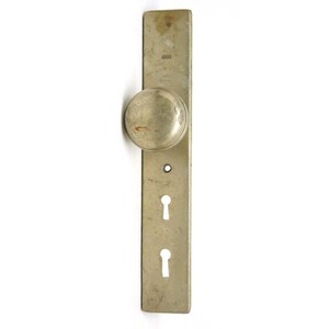 Puede incluir: Una manija de puerta vintage con un pomo redondo y dos agujeros para llaves. La manija es de metal y tiene un acabado plateado.
