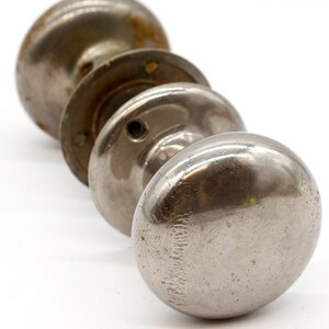 May include: Three silver door knobs with a worn finish. The knobs are round and have a smooth surface.
