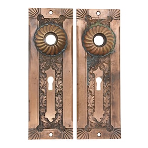 May include: A pair of antique door plates with ornate floral designs and keyholes. The plates are made of copper and have a dark patina.