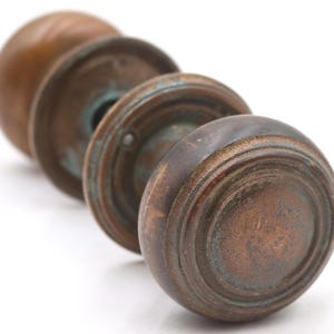 May include: Close-up of four antique bronze door knobs. The knobs are round with concentric circular ridges and a patina of verdigris. The knobs are arranged in a diagonal line against a white background.