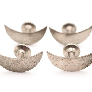 May include: Four silver-toned metal drawer knobs, each featuring a crescent moon shape. The knobs have a weathered, textured finish on the front-facing moon surface and a cylindrical post with a circular base for mounting to furniture.