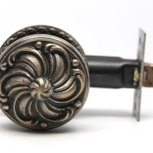 May include: A vintage door knob with a decorative, ornate, floral design. The knob is made of metal and has a brushed nickel finish.