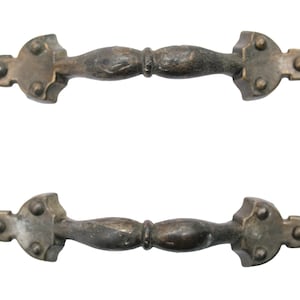 Pode incluir: Duas puxadores de porta de armário de latão antigo com um design decorativo. Cada puxador tem uma pega arredondada, ligeiramente curva com uma extremidade pontiaguda de cada lado. Os puxadores têm um aspeto desgastado e envelhecido.