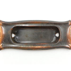 Puede incluir: Una placa de puerta de metal de color cobre vintage con un recorte rectangular para un número de casa o un nombre.