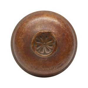 Könnte beinhalten: Eine runde Bronzeglocke mit einem dekorativen Blumenmuster auf der Oberseite.