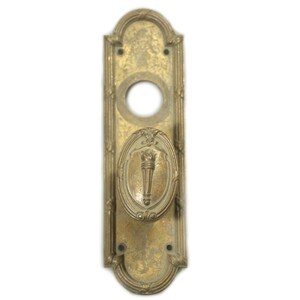 May include: Antique brass door handle with a torch design. The handle has an oval-shaped knob with a torch emblem and a rectangular backplate with decorative detailing. The finish is aged and tarnished, giving it a vintage appearance.